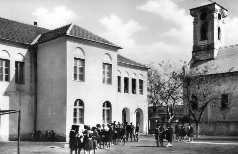 az általános Iskola (ma Dér István Általános Iskola) udvara, jobbra a Nepomuki Szent János-templom.